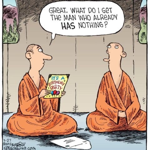 Two monks seated cross-legged indoors. One monk holds a colorful birthday card and asks a question to the other monk, who listens attentively.