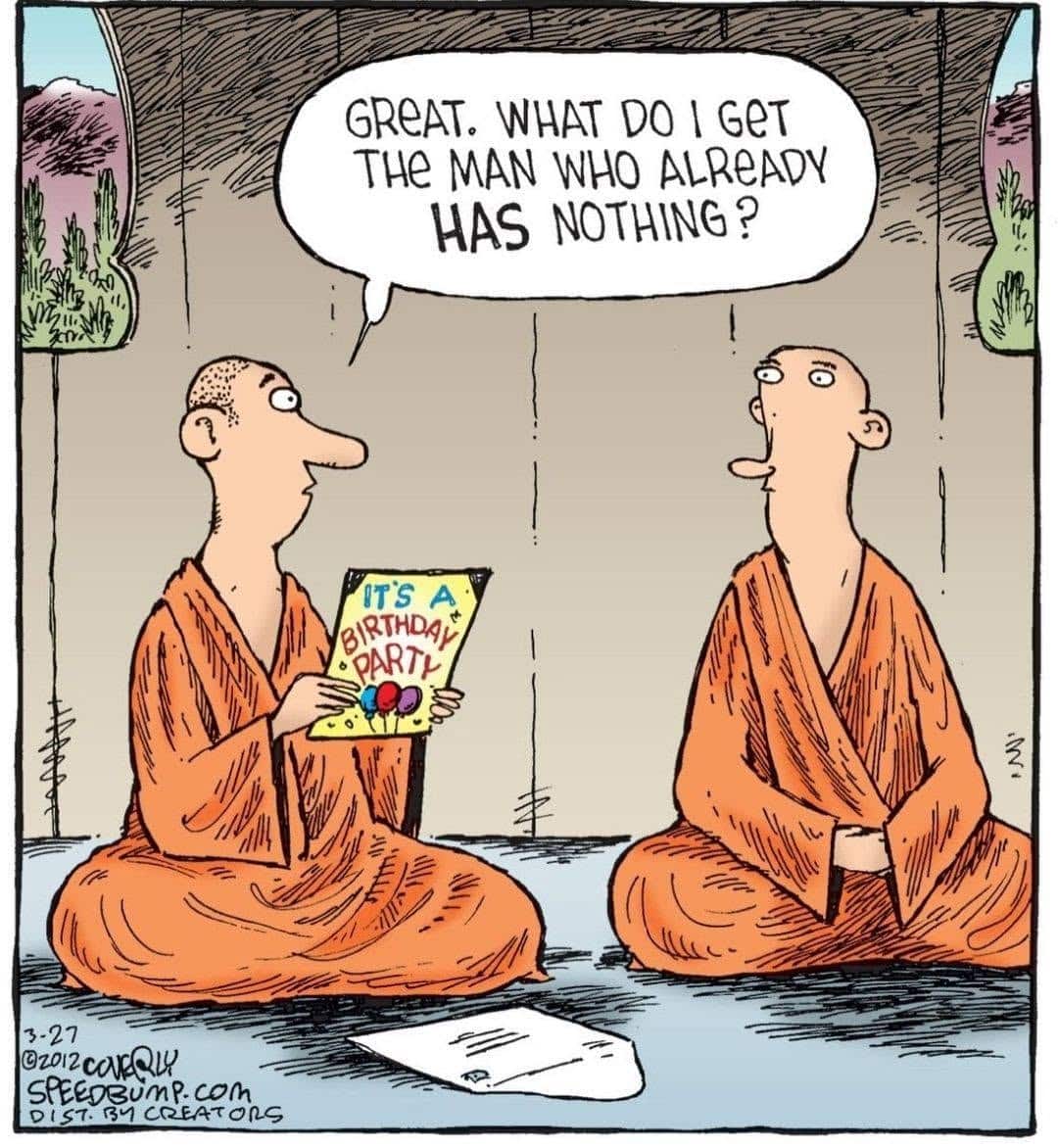 Two monks seated cross-legged indoors. One monk holds a colorful birthday card and asks a question to the other monk, who listens attentively.