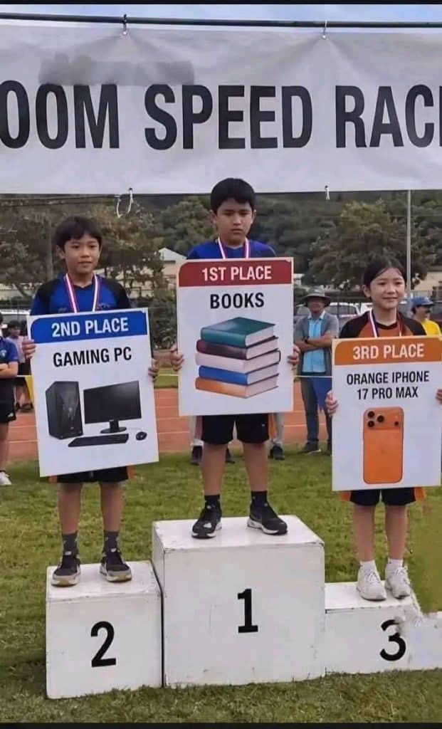 Three kids on a winners podium hold large signs showing their prizes: first place with books, second with a gaming PC, and third with an orange iPhone 17 Pro Max.