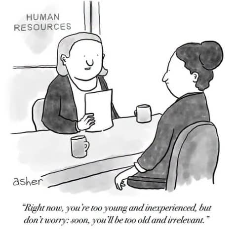 Two people sitting at a desk in a human resources office, one holding a paper and talking to the other.