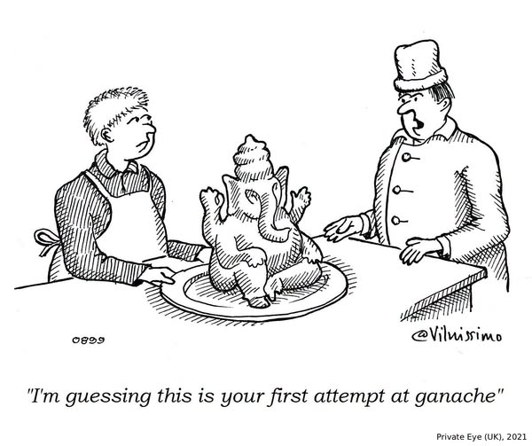 Two men stand by a table. One wears an apron and the other a chef's hat. On the table is a chocolate ganache shaped like the Hindu god Ganesha. The man in the chef's hat looks surprised and comments.