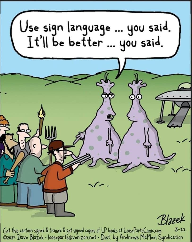 Two purple aliens with antennae stand on a grassy field. One alien has a speech bubble saying, 'Use sign language ... you said. It'll be better ... you said.' They face a mob of angry people holding weapons, with a UFO in the background.