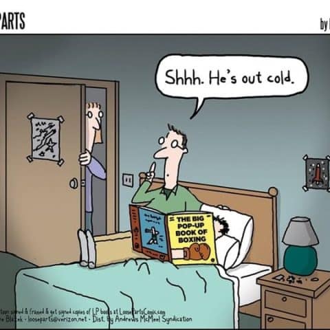 A man sitting on a bed reading 'The Big Pop-Up Book of Boxing' with a finger to his lips saying 'Shhh. He's out cold.' Another person stands in the doorway watching.