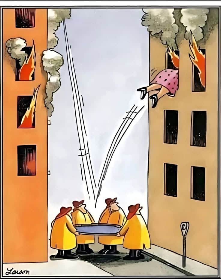Four firefighters in yellow coats holding a safety net between two burning buildings as a woman jumps out of a window.