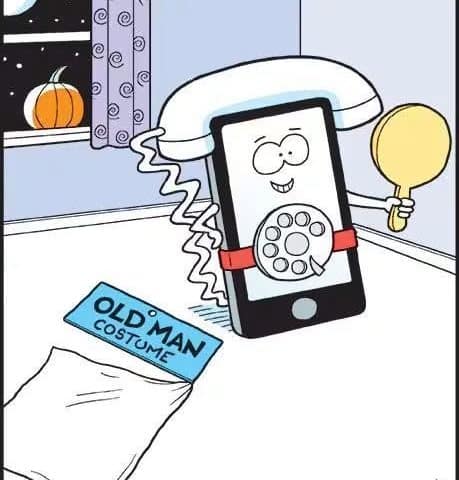 A smiling smartphone wearing a rotary phone dial and an old handset as a Halloween costume, holding a mirror, with a pumpkin on the window sill and a bag labeled 'Old Man Costume' on the floor.